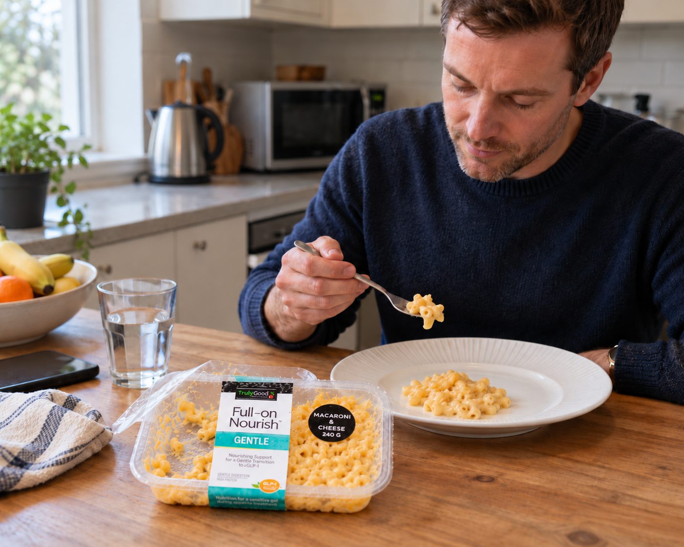 A man at his kitchen table eating Full-on Nourish macaroni and cheese, the opened tray beside his plate